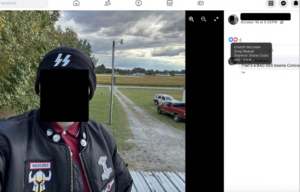 ohpeak stands facing the camera for an apparent selfie. he wears a black jacket with various skinhead/white power patches and a black beanie with nazi ss bolts on the front. he wears a red polo buttoned to the top skinhead-style. behind him are two vehicles recognizable from his father shannon dale coats's tiktok videos.